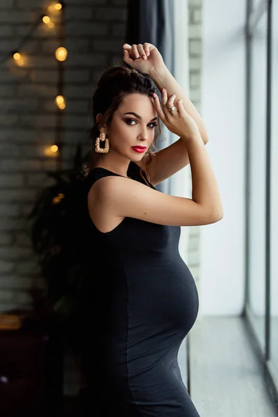 Kobiety w ciąży Europejskiej w czarnej sukni w ciemnym płaskim, kobiety w ciąży Europejskiej przebywa w pobliżu okna, stylowy i szczęśliwy Kobieta w ciąży w apartamentach, piękne kobiety w ciąży w ciemnym studiu — Zdjęcie stockowe