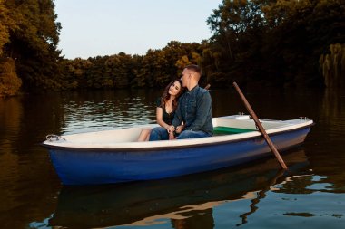 Genç Avrupalı çift gölde kayıkla geziyor, genç adam ve kız arkadaşı gün batımında teknede oturuyor, aşık çift yaz akşamları nehirde kayıkla geziyor, romantik bir randevuda mutlu bir çift.