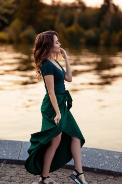 Genç Avrupalı kadın gölün yanında duruyor, doğada güzel bir Avrupalı kadın, nehrin kenarında yeşil elbiseli güzel bir kadın.