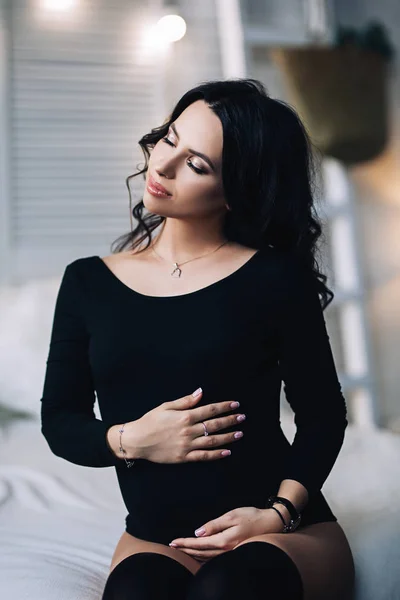 Беременная европейская женщина в белой квартире, молодая европейская женщина ждет ребенка, беременная женщина с черными волосами в черной одежде в светлой квартире — стоковое фото