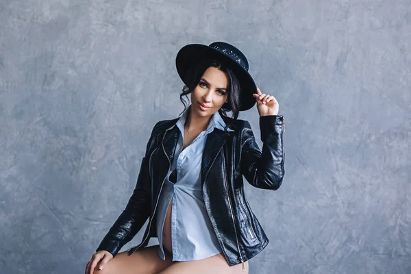 Pregnant european woman in gray apartment, young european woman waiting for a child, prenant woman with black hair in a blue shirt and black jacket with hat — Stock Photo, Image