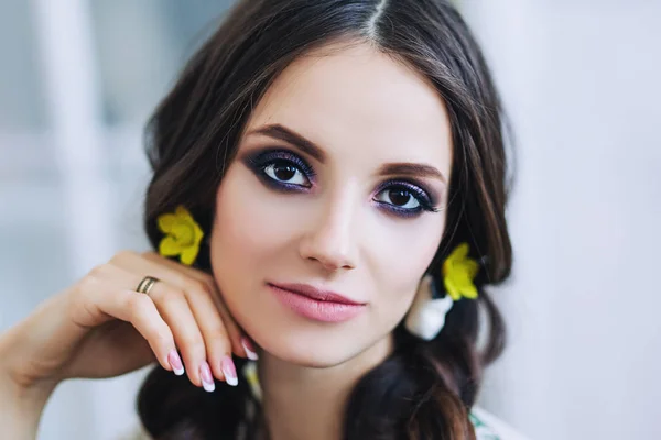 Portrait of beautiful european woman in yellow earings in white apartment, pretty young woman with dark hair in light apartment