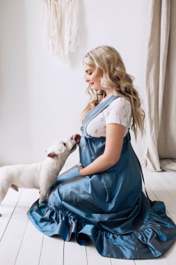 Beyaz dairede köpeği ile hamile Avrupalı kadın, bir çocuk bekleyen Avrupalı kadın, beyaz daire uzun mavi elbiseli açık saçlı prenant kadın, güzel güzel gelecek anne ile