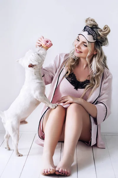 Beautiful european woman with her dog in white apartment, european woman is playing with her white dog, pretty woman with light hair in silk pijamas in white apartment, beautiful pretty woman with