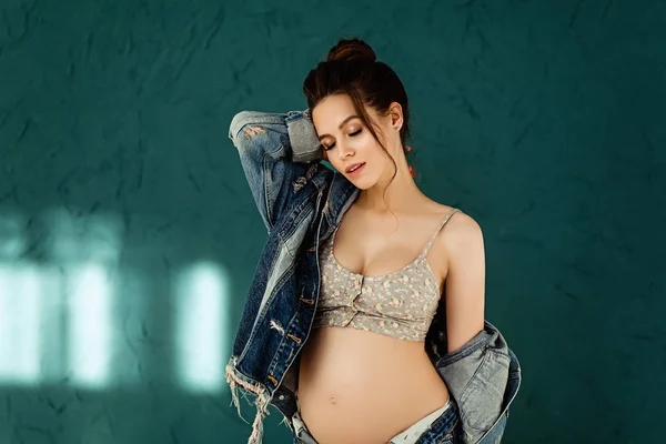 Femme européenne enceinte sur fond bleu, belle jeune femme européenne attendant un enfant, femme prenant avec les cheveux foncés en jeans est fille regardant vers le bas — Photo