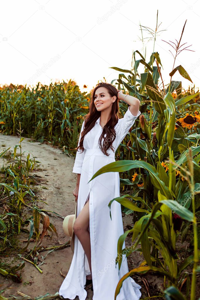 Pregnant european woman in a field of sunflowers, beautiful young european woman waiting for a child, prenant woman with dark hair in white long dress with hat on the nature
