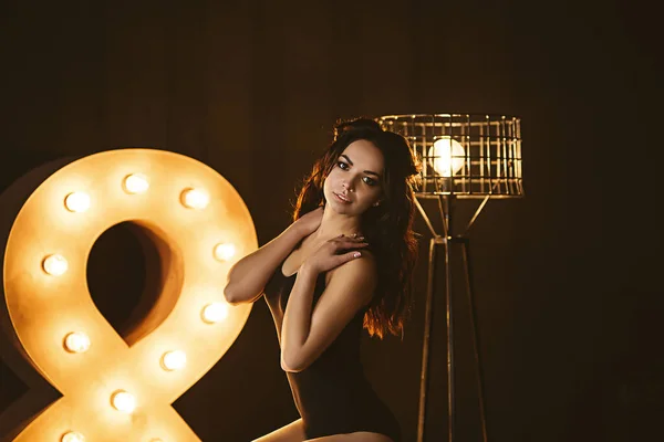 Portrait of young european woman in dark studio with lights, pretty caucasian lady in black wear and knee socks with long dark hair and bright makeup, she is sitting on the floor — Stock Photo, Image