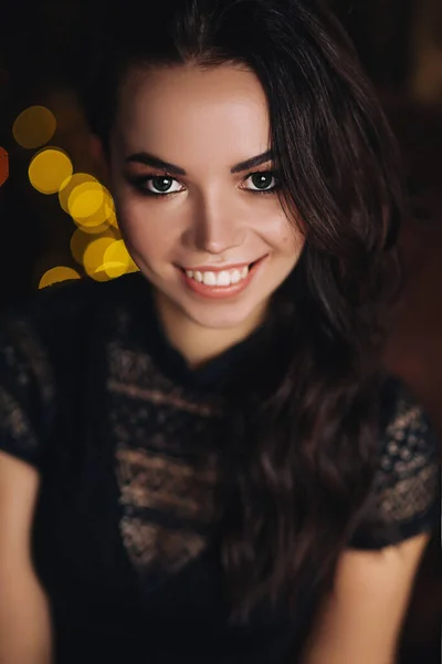Portrait de jeune femme européenne en studio sombre avec des lumières, jolie dame caucasienne en tenue noire avec de longs cheveux foncés et un maquillage lumineux, elle sourit — Photo