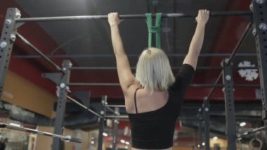 Barfiks çekmek yapan sarışın sporcumuz, portresi açık modern bir spor salonu barda.