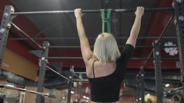 Retrato de la deportista rubia, que está haciendo barbilla-ups en el bar en el gimnasio moderno . — Vídeo de stock