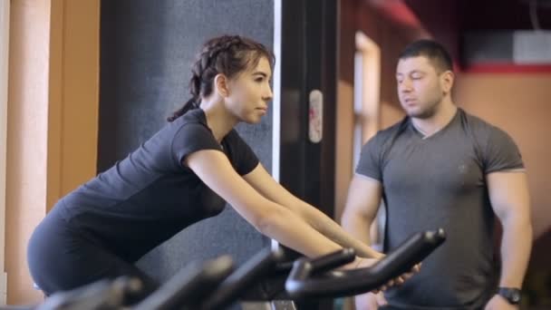 Személyi edző órák, mint egy nő végez terhelési szobabicikli. — Stock videók