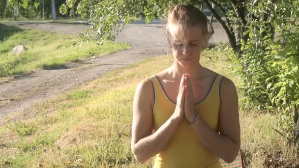Жінка стоїть із закритими очима, тримаючи складені руки в природі на відкритому повітрі — стокове відео