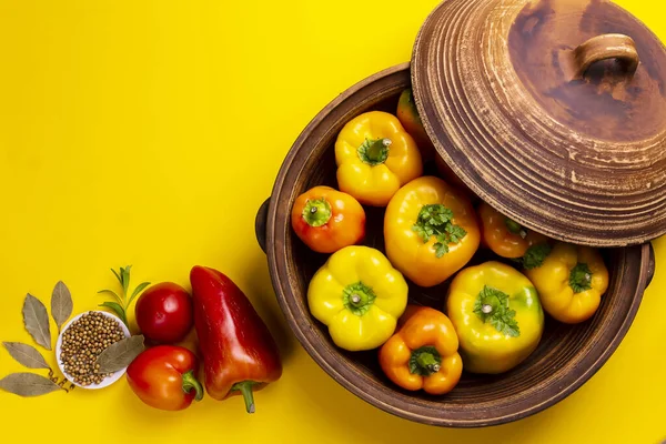 Paprika kuning segar dengan tomat dan rempah-rempah dalam piring dalam panci tanah liat dengan latar belakang kuning. — Stok Foto