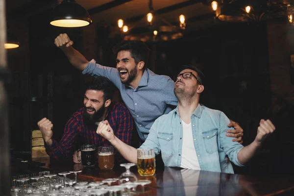 The guys in the pub drink beer and watch the football match