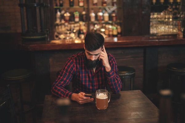 Young handsome man with beer using mobile in pub
