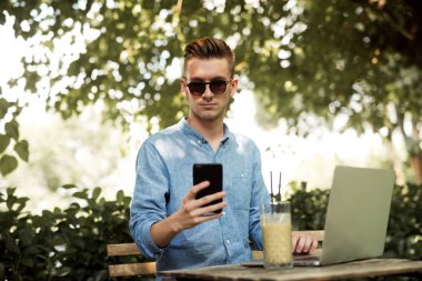 Açık kafede oturan smartphone ile genç adam