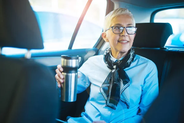 Woman sitting in the back seat of the car and drinking coffee
