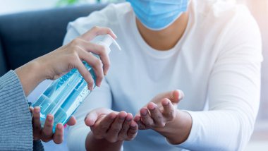 El temizliği için yüz maskesi takan iki adamın avuçlarına alkol pompalarken yakın çekim. Önce güvenlik, mikrop, bakteri ya da virüs için koruma.