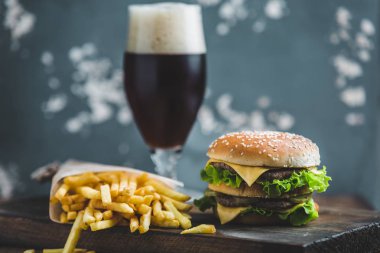 Burger patates ve bir ahşap tahta bir mavi-gri arka plan üzerinde koyu bira