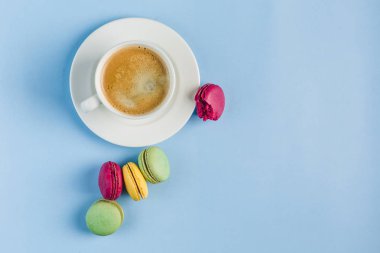 Mavi sırt üzerinde beyaz bir fincan kahve ile çok renkli macaroons