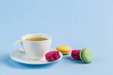 Mavi bir backgrou üzerinde kahve beyaz bir Fincan ile renkli macaroons