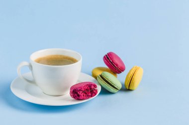 Mavi bir backgrou üzerinde kahve beyaz bir Fincan ile renkli macaroons