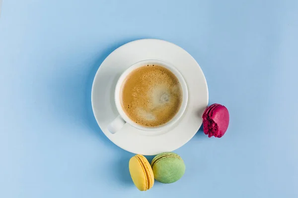Bunte Makronen mit einer weißen Tasse Kaffee auf blauem Rücken — Stockfoto
