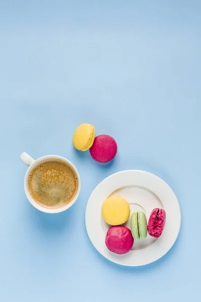 Bunte Makronen mit einer weißen Tasse Kaffee auf blauem Rücken — Stockfoto