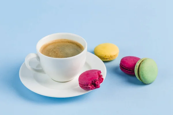 Bunte Makronen mit einer weißen Tasse Kaffee auf blauem Hintergrund — Stockfoto