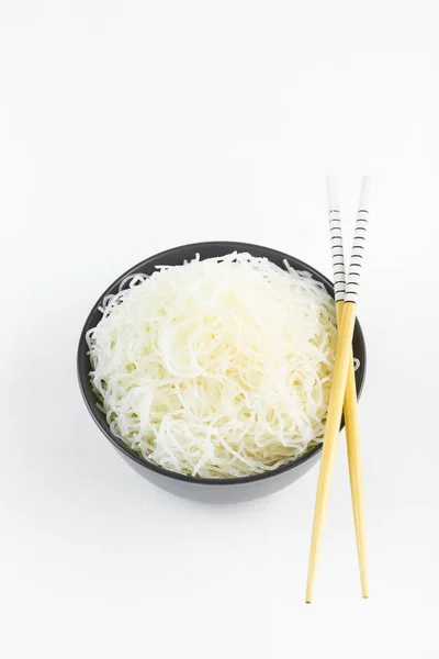 Fideos de arroz celofán en un tazón negro con palillos en blanco — Foto de Stock