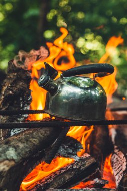 Ateşin üstünde çaydanlık. Vahşi doğadaki bir turist kampında çok güzel bir kamp ateşi. Ormanda hayatta kalmak. Ateşin üstünde çaydanlık. Ağaçlardaki yangından çıkan duman. Ateşte pişirmek için fırın..