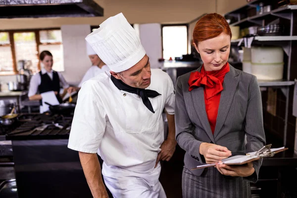 女经理和男厨师在酒店厨房的剪贴板上写字 — 图库照片