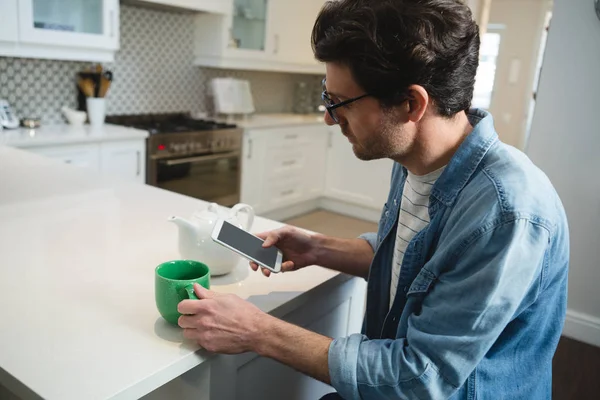 男子在厨房里喝咖啡时使用手机 — 图库照片