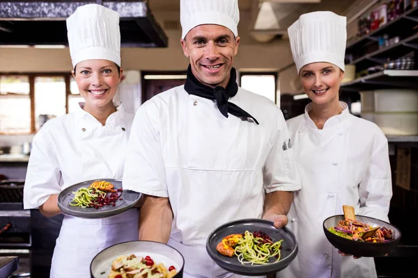 ホテルのキッチンで調理された食べ物のプレートを保持しているシェフのグループ — ストック写真