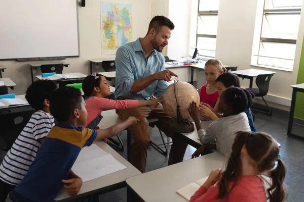 Male teacher teaching his kids about geography by using globe in classroom of elementary school