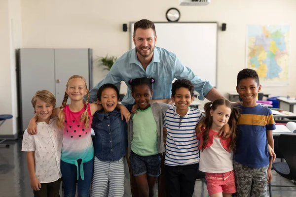 Happy school kids and teacher standing and looking at camera in classroom of elementary school