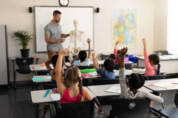 Bakifrån Skolbarnen Höja Handen Och Sitter Vid Skrivbord Grundskolan — Stockfoto