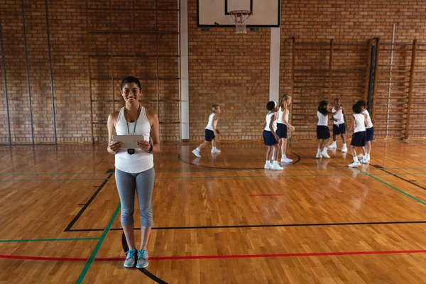 Front view of smiling female basketball coach with digital tablet looking at camera at basketball court