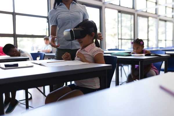 Side view of school girl using virtual reality headset at desk in classroom of elementary school