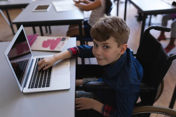 一个残疾小学生坐在小学教室的办公桌前学习笔记本电脑的高角度视图 — 图库照片