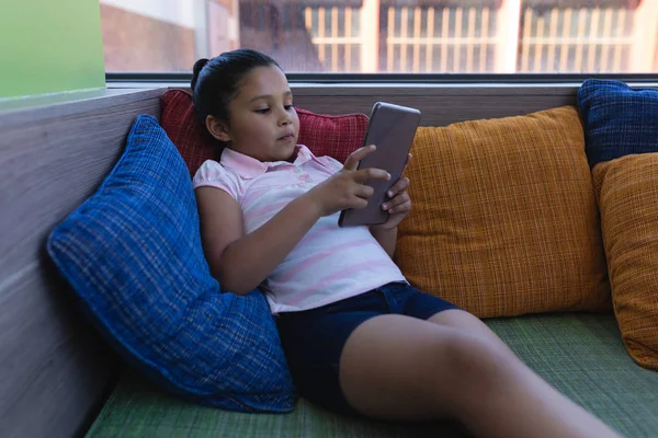 女子高生は 学校図書館のソファに立地しながらデジタル タブレットの勉強の正面図 — ストック写真