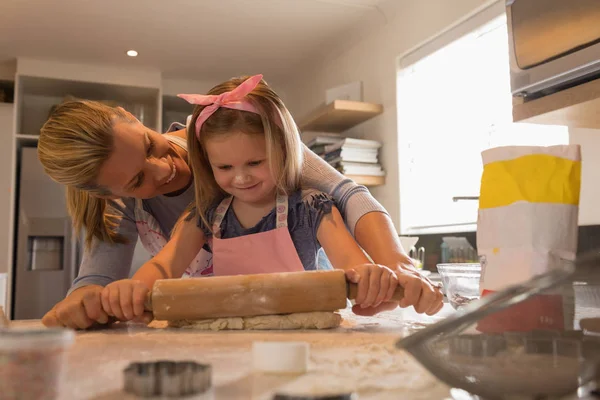 自宅のキッチンでクッキー生地を伸ばして彼女の娘を助ける母の正面図 — ストック写真