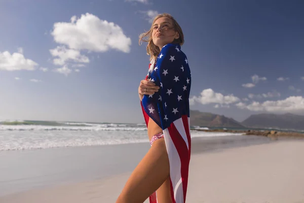 晴れた日にビーチにアメリカの国旗に包まれた若い女性の側面図 — ストック写真