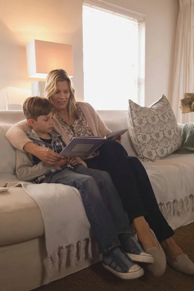 自宅のリビング ルームで絵本を読みながら一緒に時間を過ごす彼女の息子を持つ魅力的な母の側面図 — ストック写真