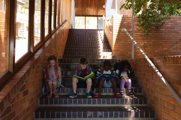 Pohled Zepředu Schoolkids Čtení Kniha Mezi Spolužáky Zatímco Sedí Schodech — Stock fotografie