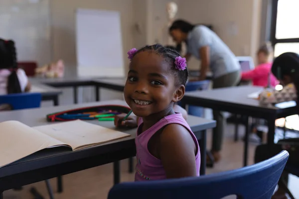 Vista Trasera Sonriente Colegiala Sentada Escritorio Mirando Cámara Aula Escuela —  Fotos de Stock