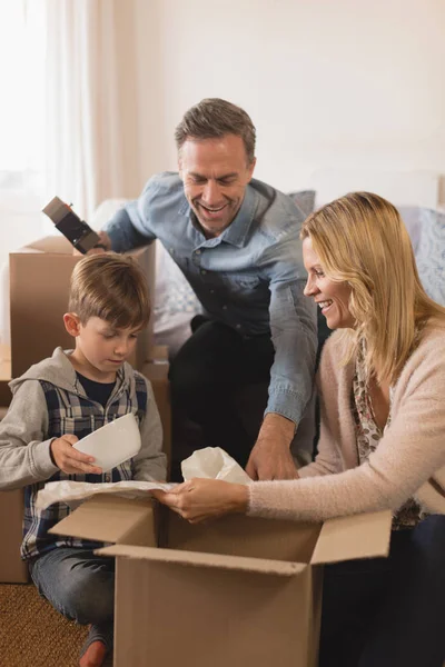 彼らの新しい家にボックスを段ボールを開梱しながら一緒に時間を過ごす幸せな家族の側面図 — ストック写真