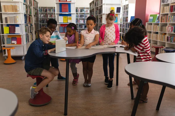 Front view of group of schoolkids studying together at table in school library