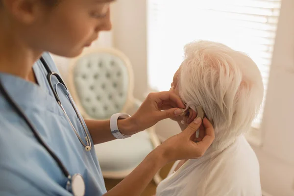 Vrouwelijke Arts Invoegen Gehoorapparaat Senior Vrouw Oor Thuis — Stockfoto