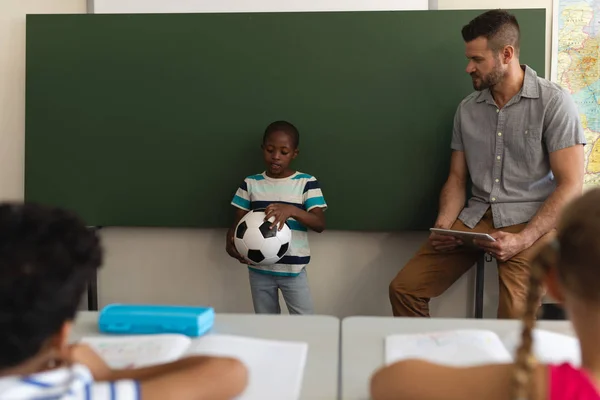 黒の少年サッカーを押し 小学校の教室で緑のボードに立っての正面図 — ストック写真